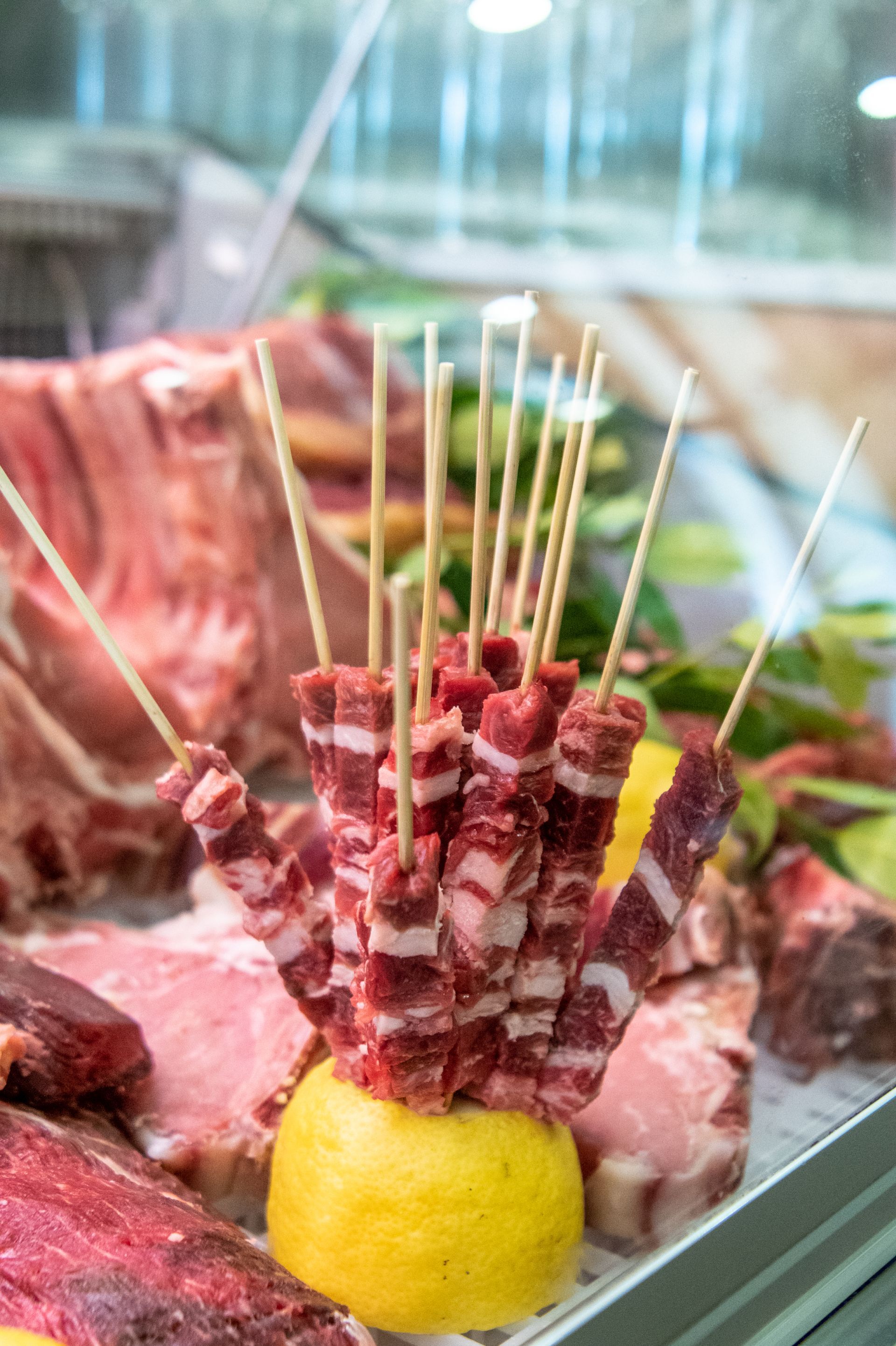 Spiedini di carne grigliata disposti intorno a un limone su un vassoio di vetro.