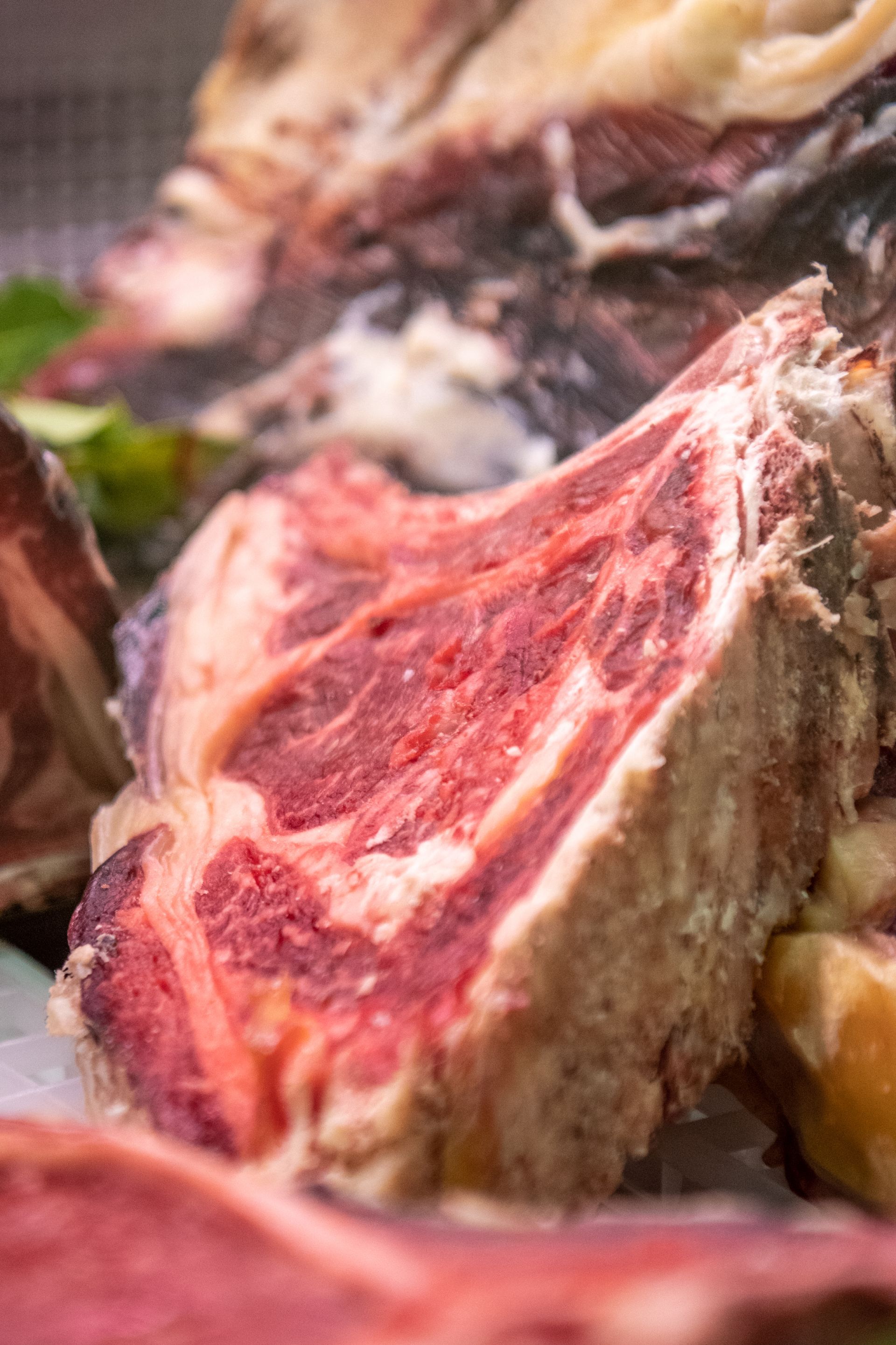 Primo piano di una bistecca cruda, marezzata, con grasso rosso e bianco, su un piatto.
