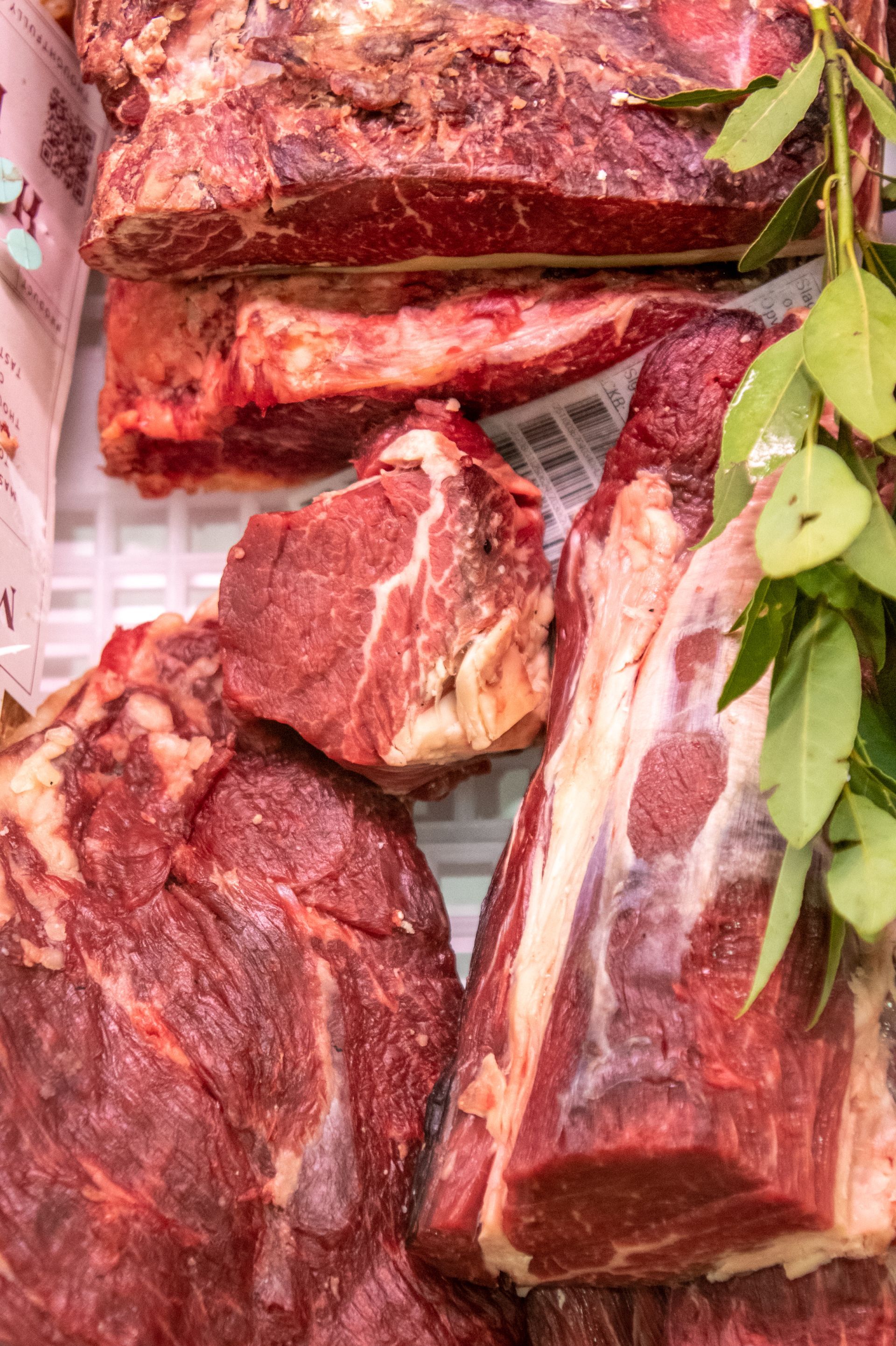 Tagli di manzo crudo esposti su un vassoio da mercato, con verdure a foglia verde nelle vicinanze.