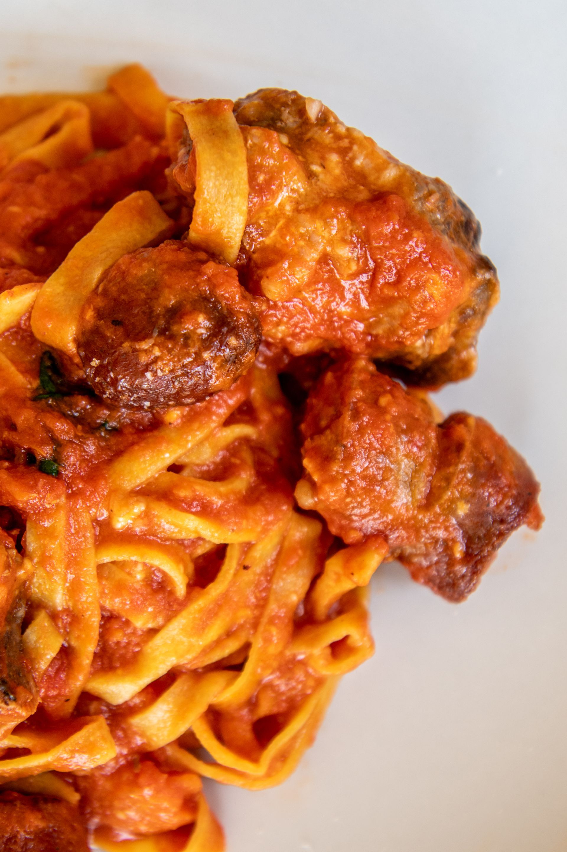 Primo piano di spaghetti al sugo di pomodoro con pezzi di carne rosolata su un piatto bianco.