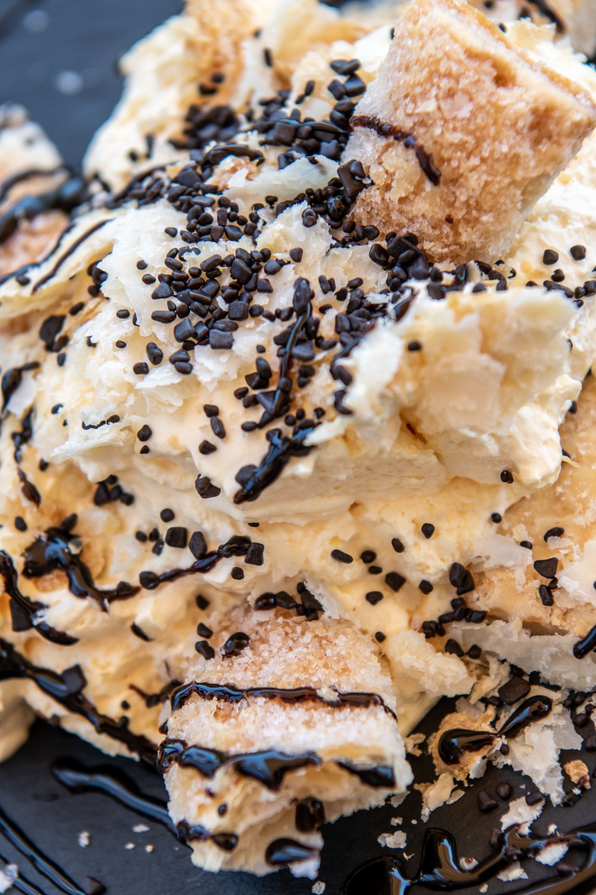 Dessert di gelato con glassa al cioccolato e granella, servito in una ciotola nera.