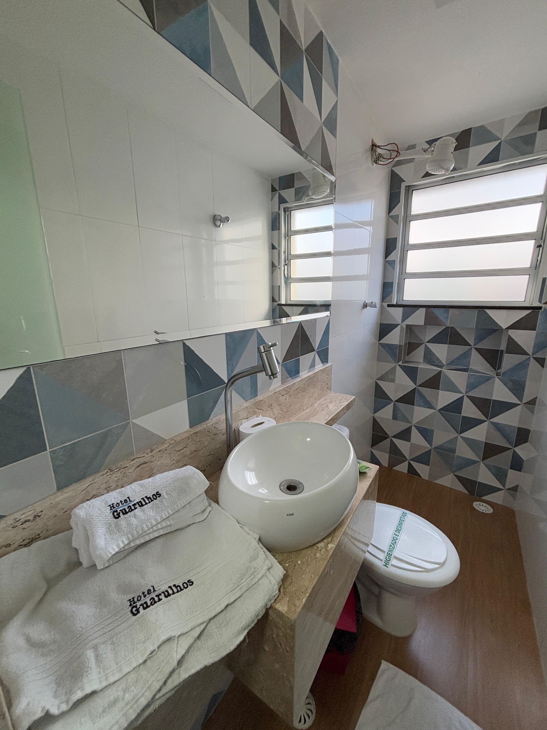 Um banheiro moderno com uma pia de apoio branca sobre uma bancada de granito, azulejos de parede com padrões geométricos e um vaso sanitário branco.