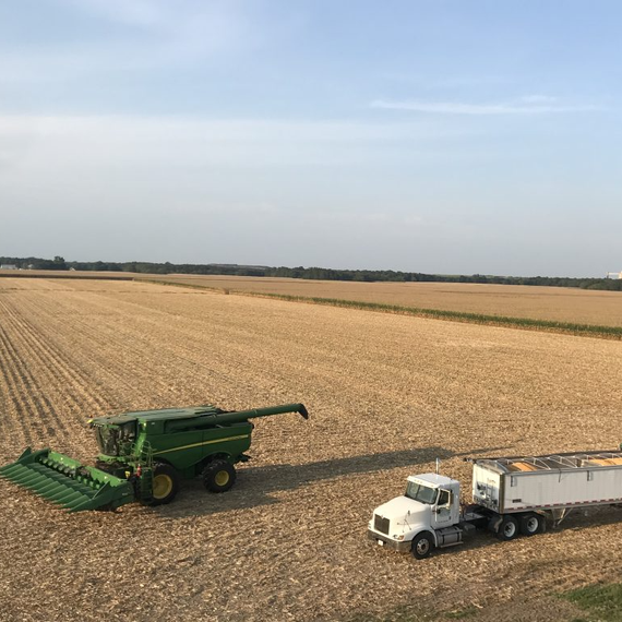 Combine harvester and white truck in a vast harvested field under a clear sky