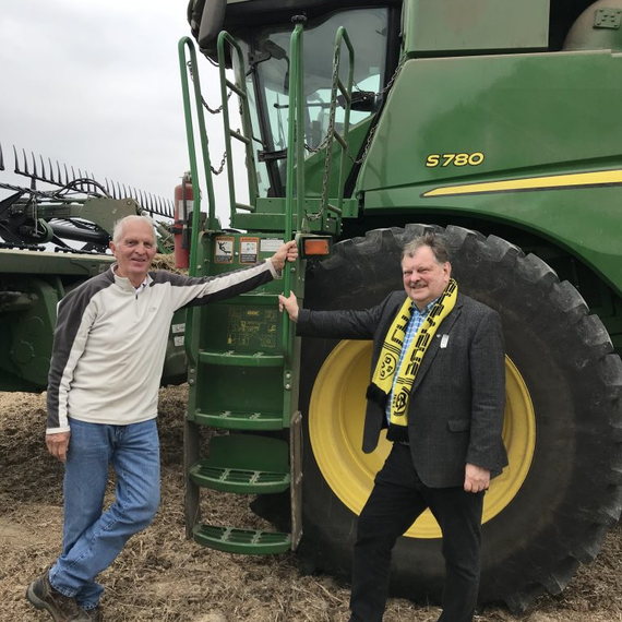 Two men standing beside a green John Deere tractor, smiling and leaning on its ladder.