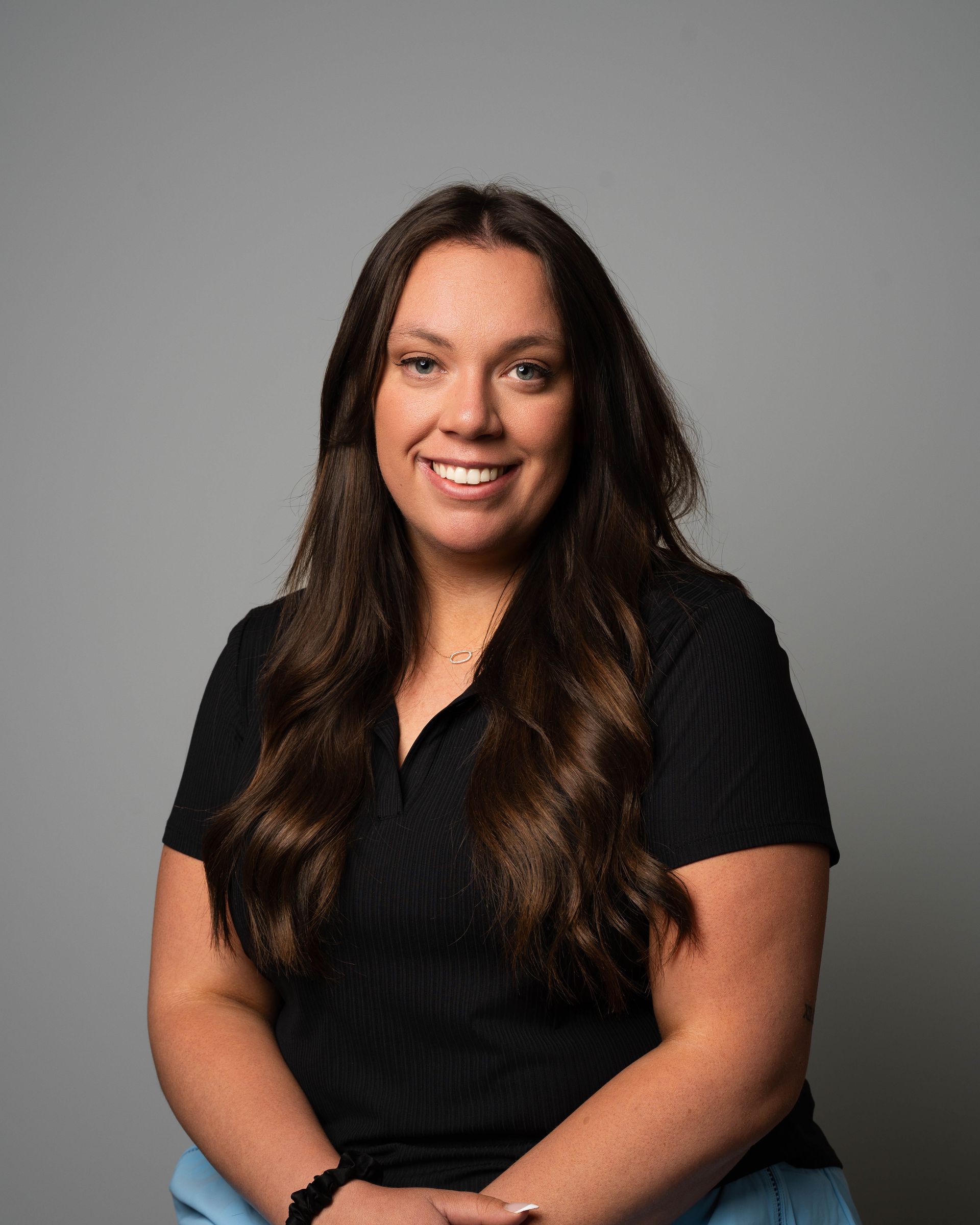 Smiling woman with long dark hair in a black shirt against a gray studio backdrop