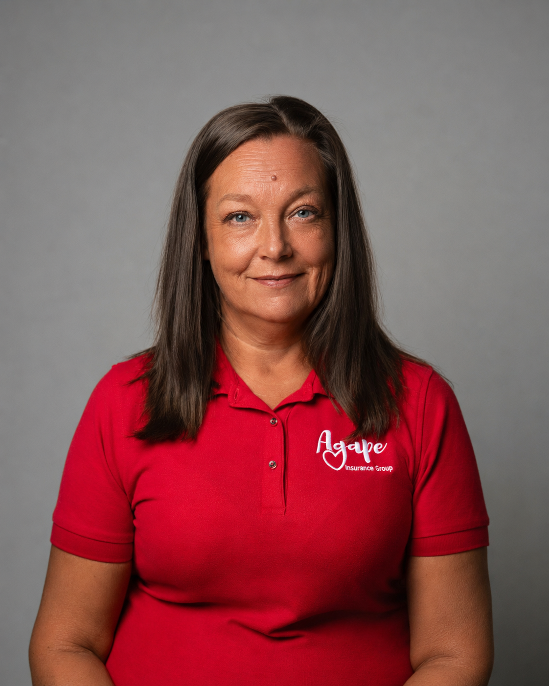A woman wearing a blue shirt and a necklace is smiling for the camera.