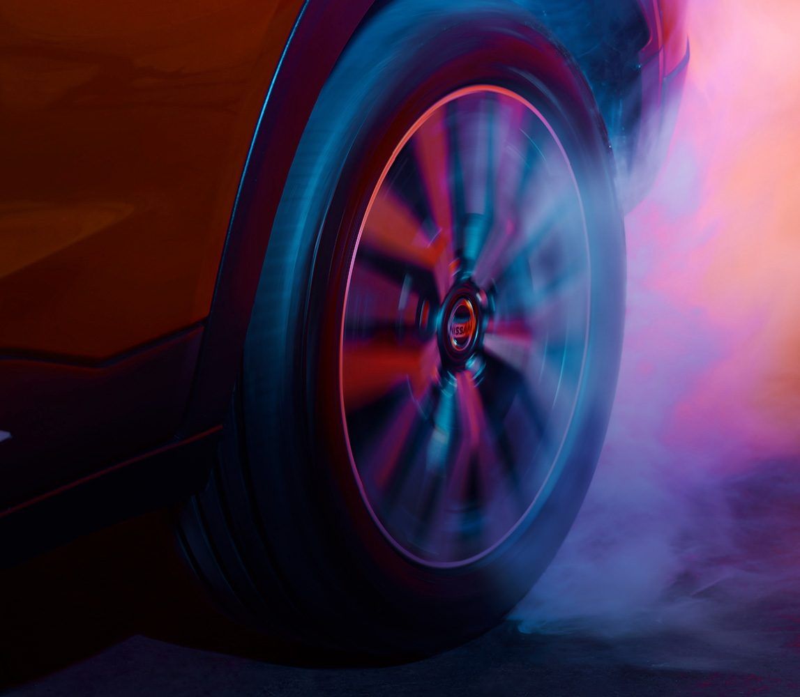 Primer plano de una rueda de coche girando entre humo de colores rosa y azul.