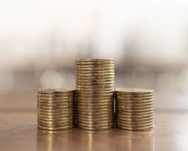 Tres pilas de monedas de oro sobre una superficie de madera, con la pila central más alta y el fondo desenfocado.