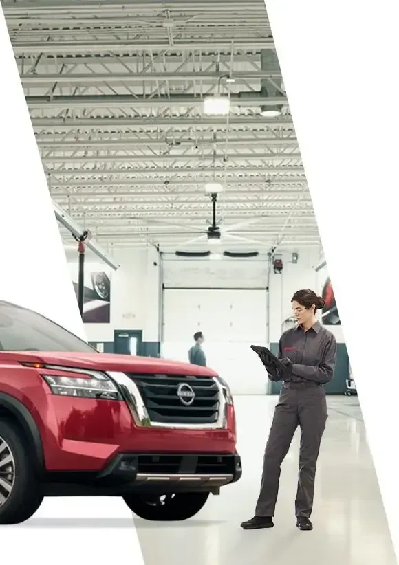 Un SUV Nissan rojo en un garaje bien iluminado, con un mecánico de pie cerca sosteniendo un portapapeles.
