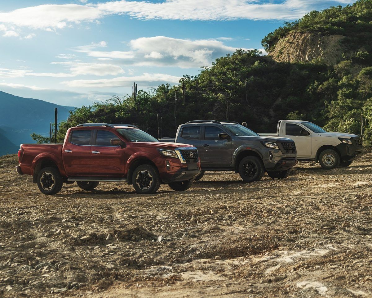 Tres camionetas estacionadas en un mirador rocoso con montañas y cielo azul al fondo.