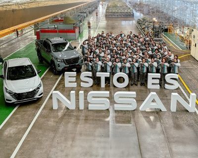 Grupo de personas y coches en una fábrica con grandes letras que dicen “ESTO ES NISSAN” en el suelo.