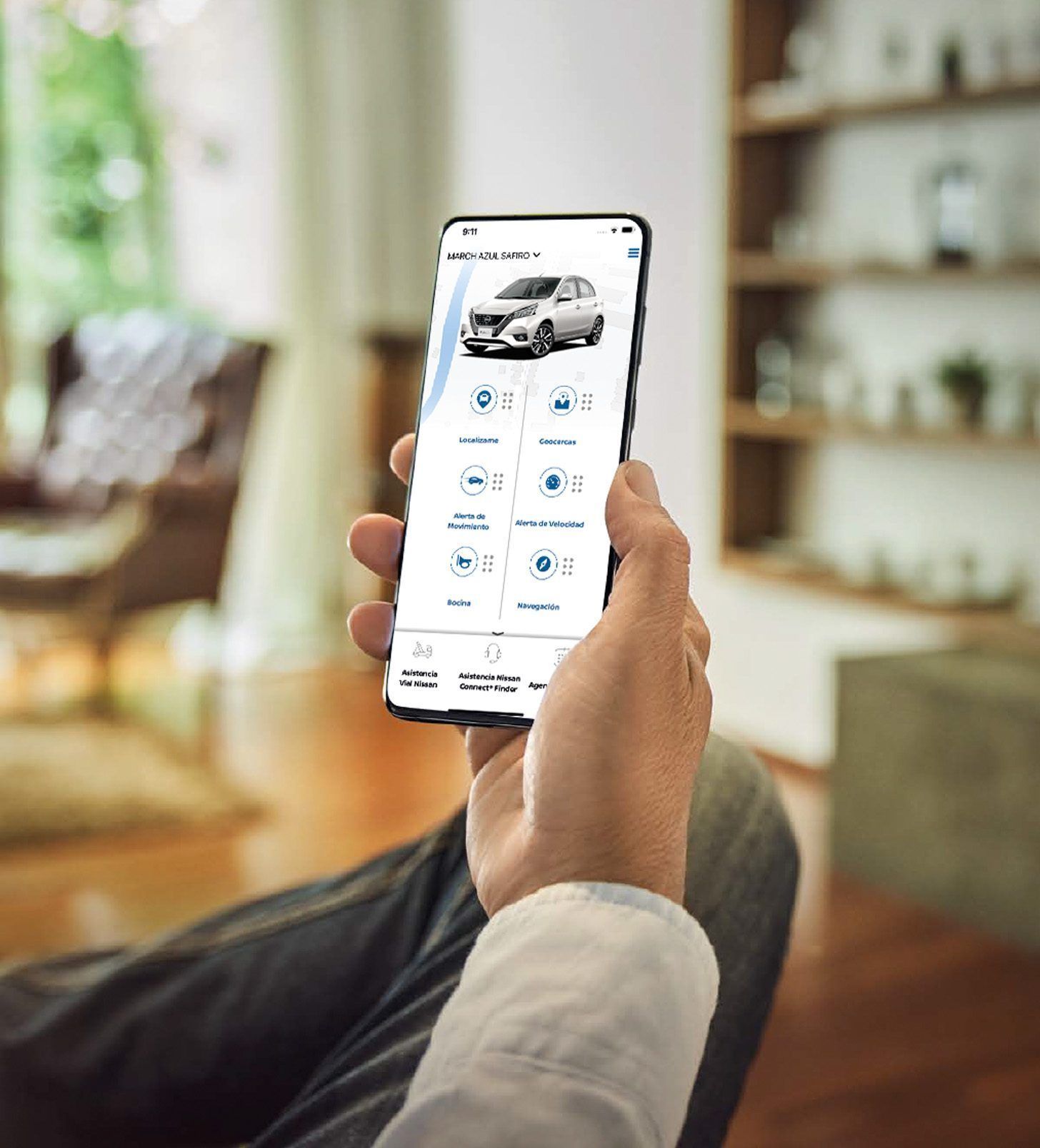 Una mano sostiene un teléfono inteligente que muestra una aplicación de automóviles en una sala de estar luminosa.