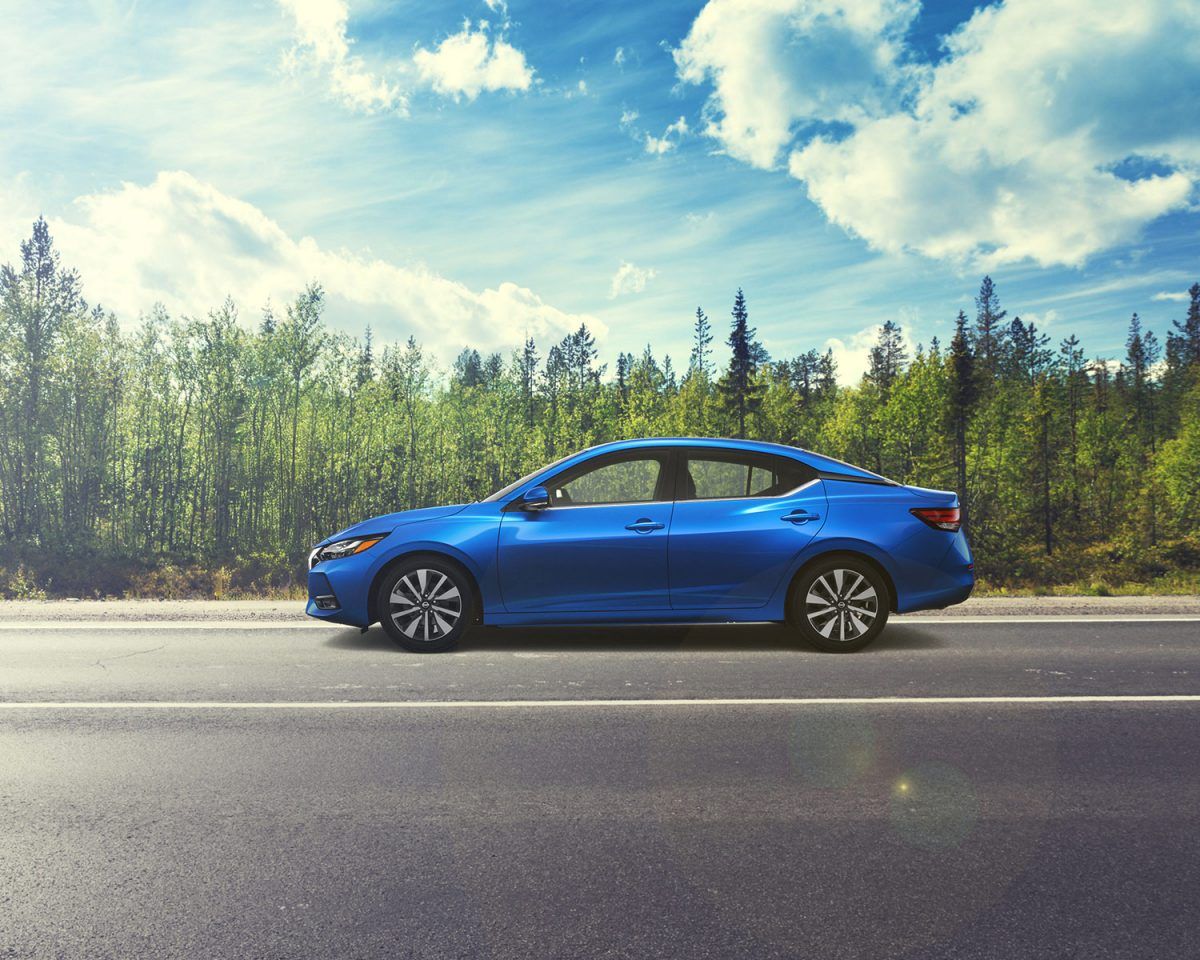 Un sedán azul estacionado al borde de la carretera con árboles y cielo nublado al fondo.