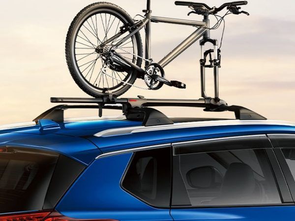 Bicicleta plateada montada en la baca de un coche azul contra el cielo del atardecer.