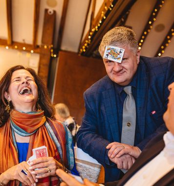 Woman laughing, man with playing card on forehead; indoor event. magic wedding entertainment eddie young