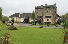 Stone building with a square tower, set in a grassy yard. Gray sky and flowers in the foreground.
