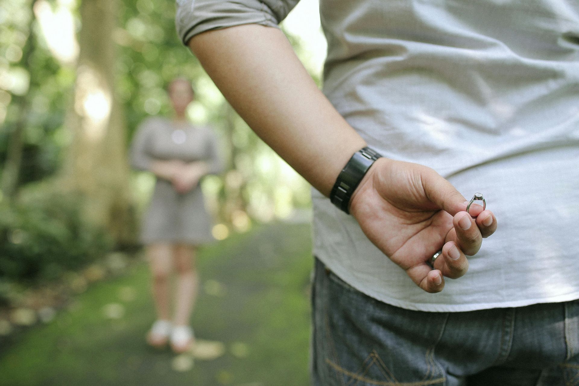 Man with ring behind his back, approaching woman in a park, preparing to propose.