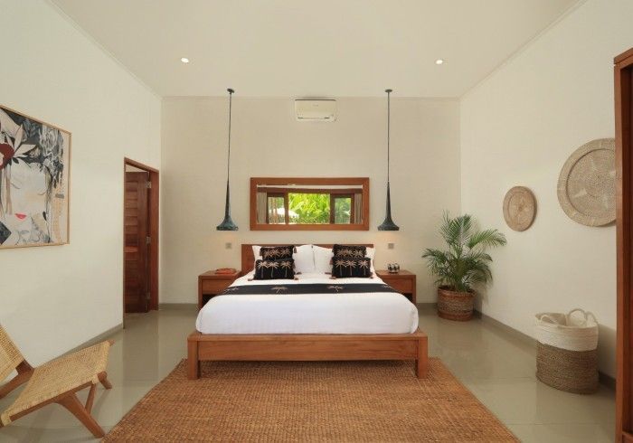 Bedroom with wooden bed, brown rug, and artwork. Natural light streams from window.