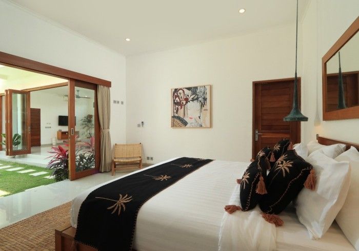 Bedroom with open doors to a patio. White walls, wood accents, king-size bed, artwork, and a small chair.