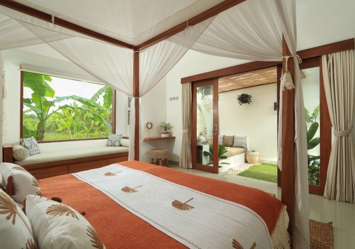 Bedroom with four-poster bed, window seat, and sliding doors to a patio overlooking lush greenery.