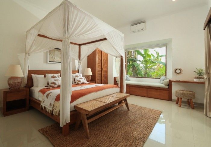 Bedroom with four-poster bed, window seat, wooden furniture, and neutral decor.