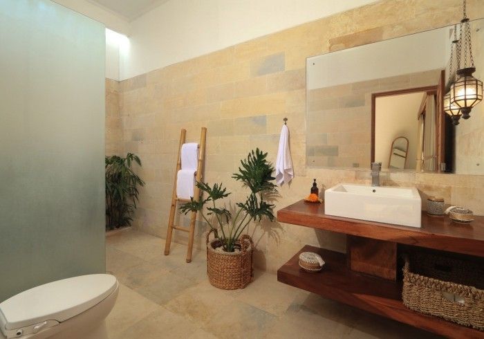 Bathroom with stone walls, wooden vanity and accents, toilet, and plants.