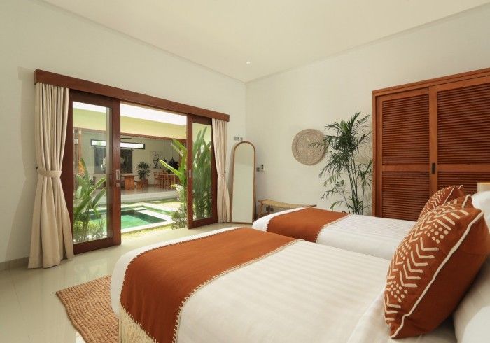 Bedroom with two twin beds, sliding doors open to a pool. Earth tones, natural light.