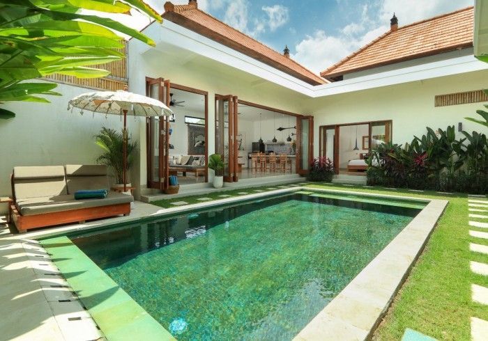 Pool and patio of a villa with an open dining area and a lounger under a parasol.
