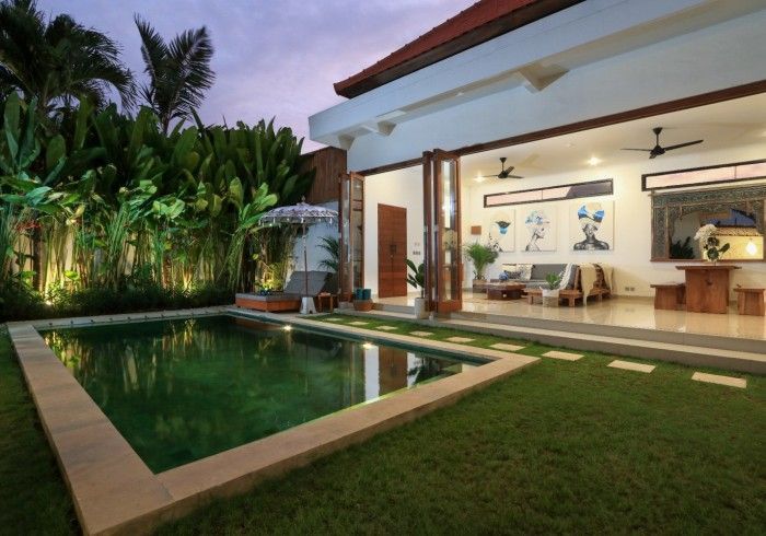 Poolside villa with a pool, lawn, and open-plan living area at twilight.
