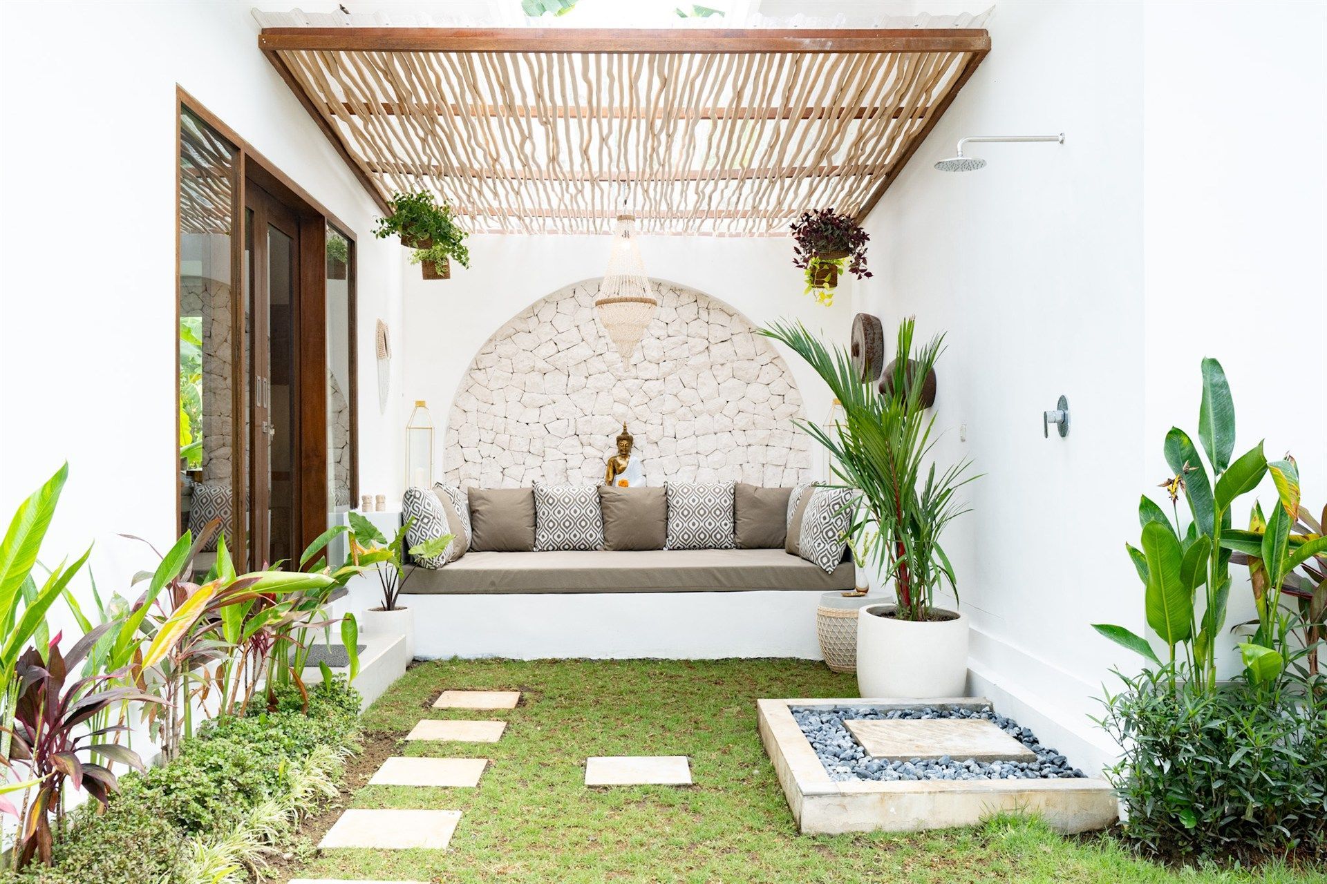 Outdoor oasis with seating area, plants, and grass pathway. White walls, bamboo roof, and stone details.