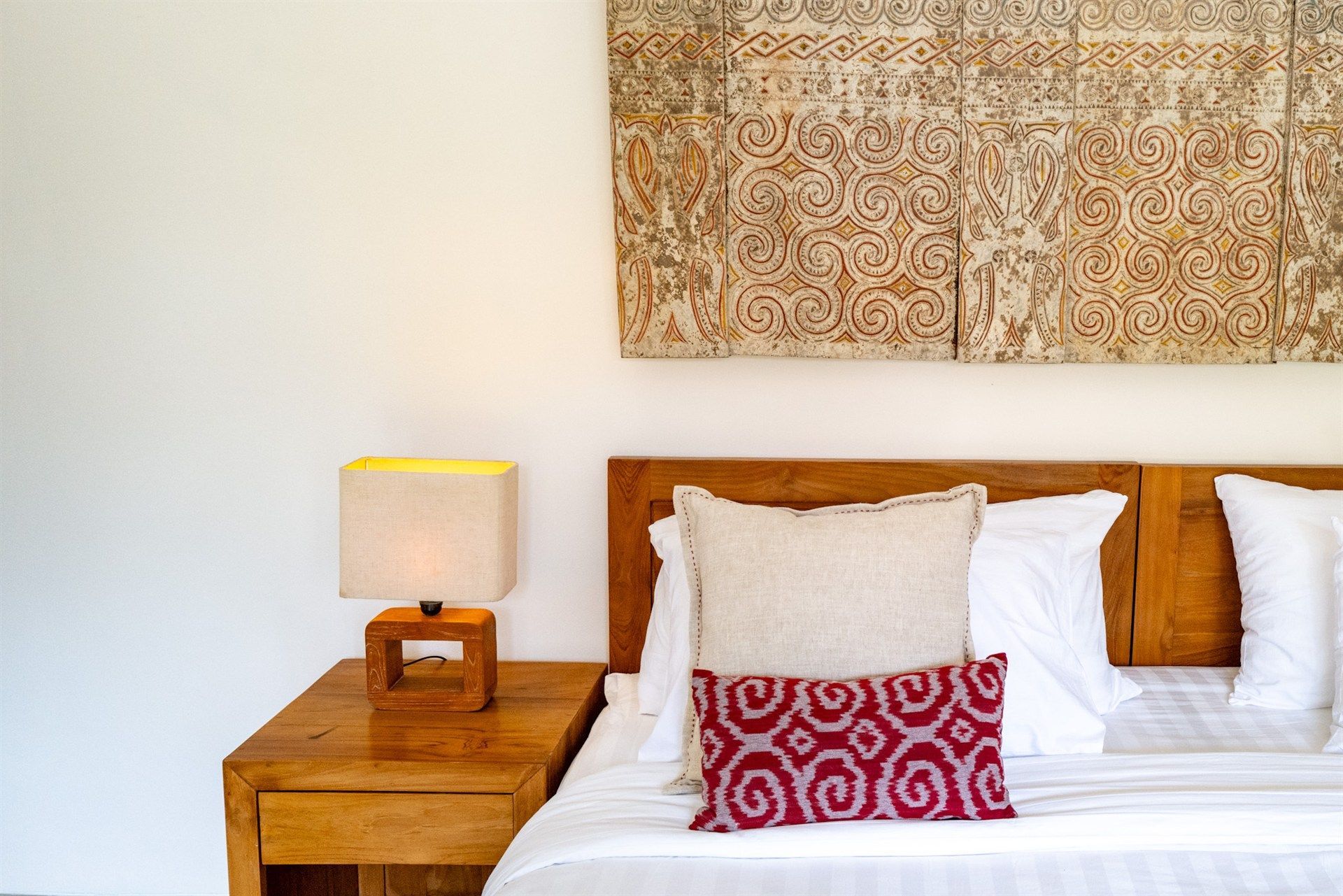 Bedroom with a wooden headboard, nightstand, and decorative panel. White bedding, pillows, and a patterned cushion.
