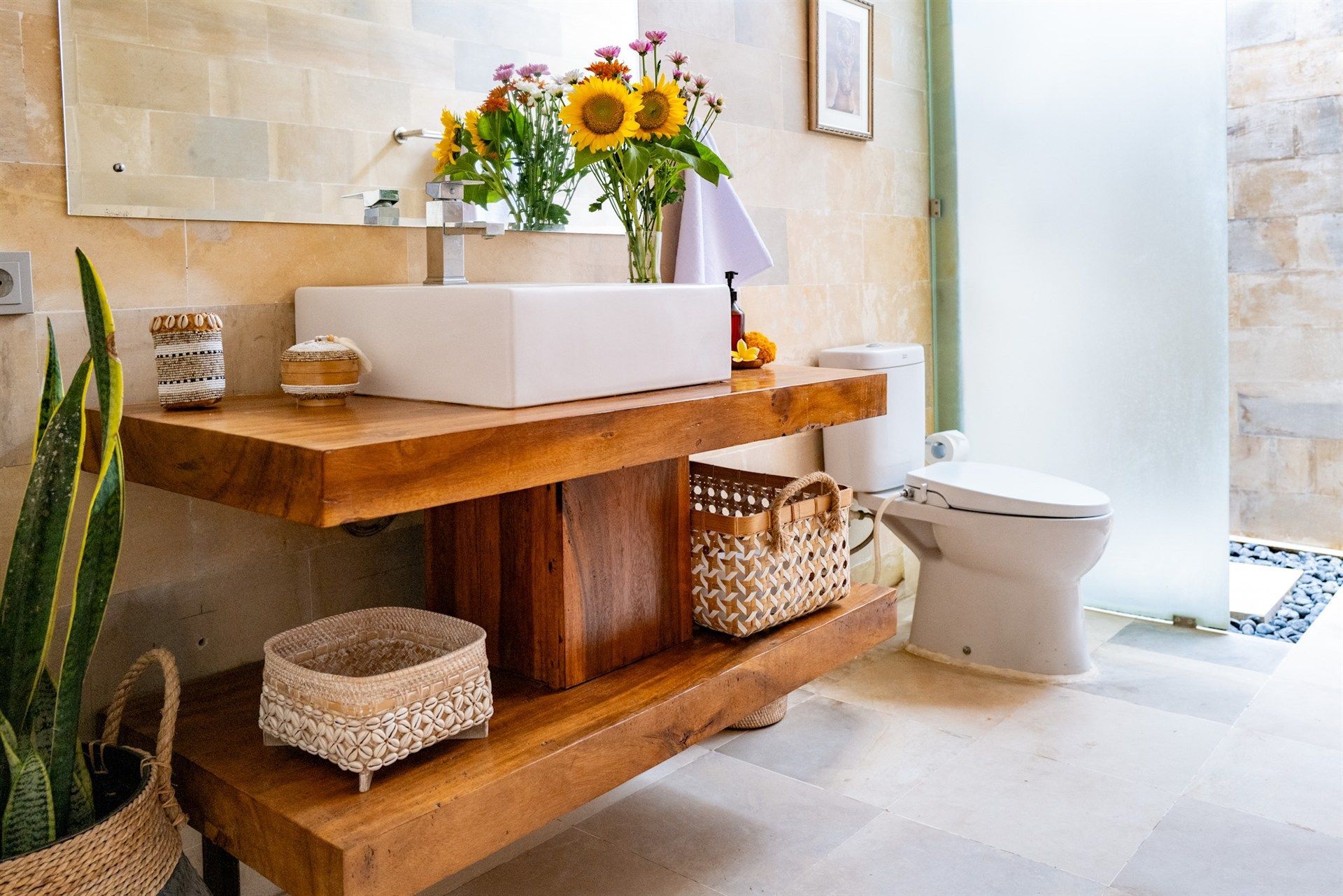 Bathroom with a wooden vanity, rectangular white sink, toilet, and a glass shower door. Sunflowers are in a vase.