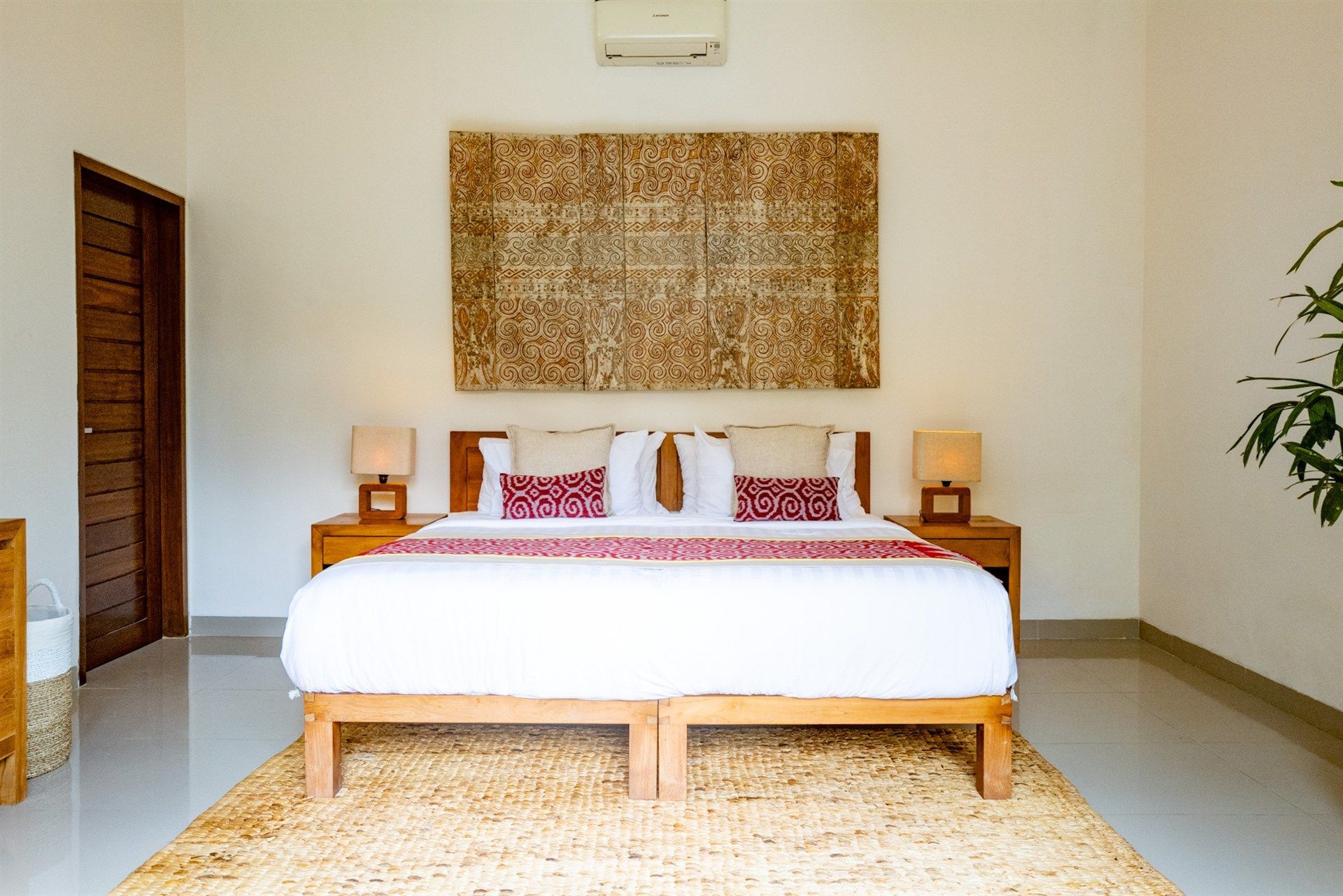 Bedroom with a bed, nightstands, rug, and art piece, against a white wall.