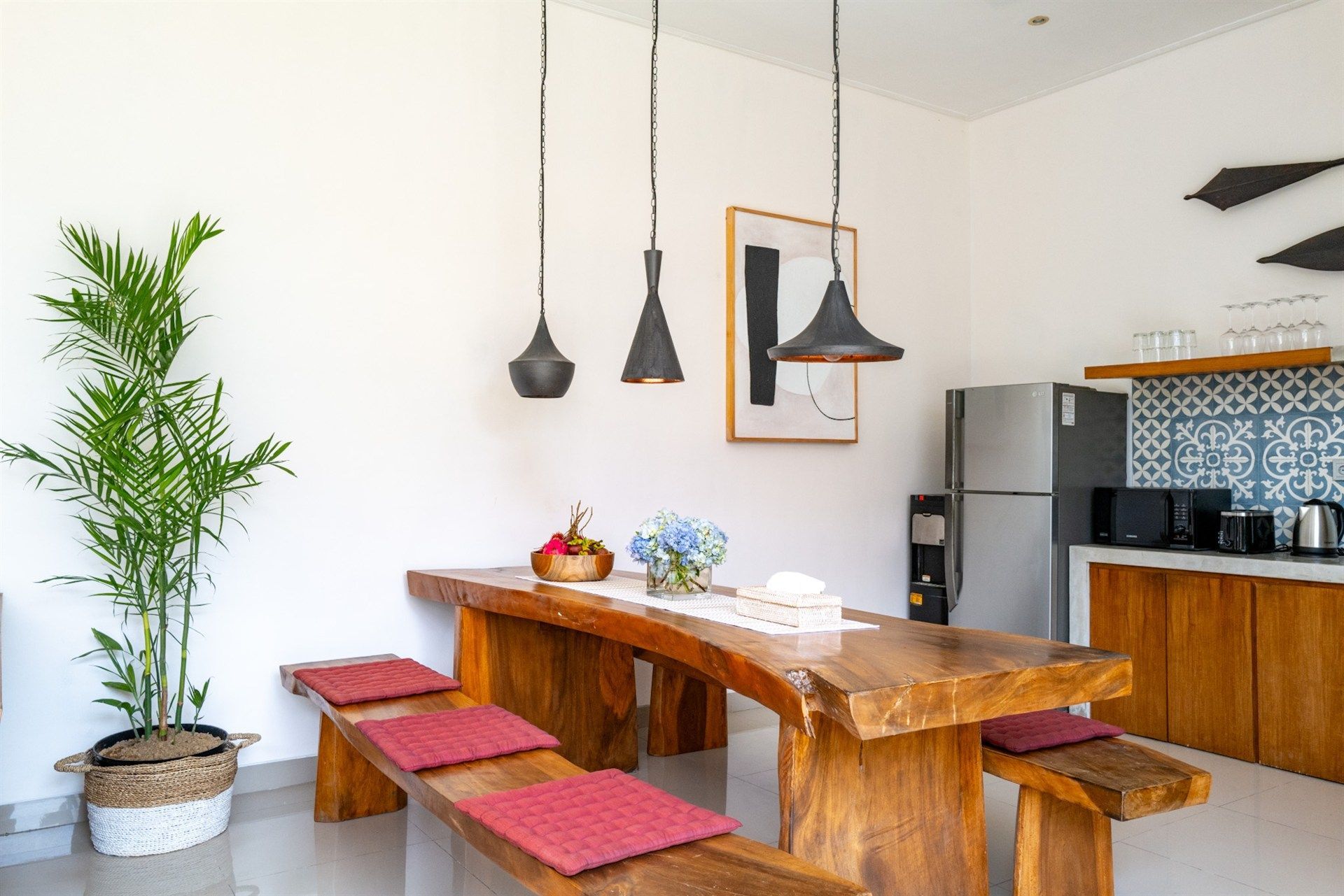 Dining area with wooden table, benches, pendant lights, and kitchen appliances.