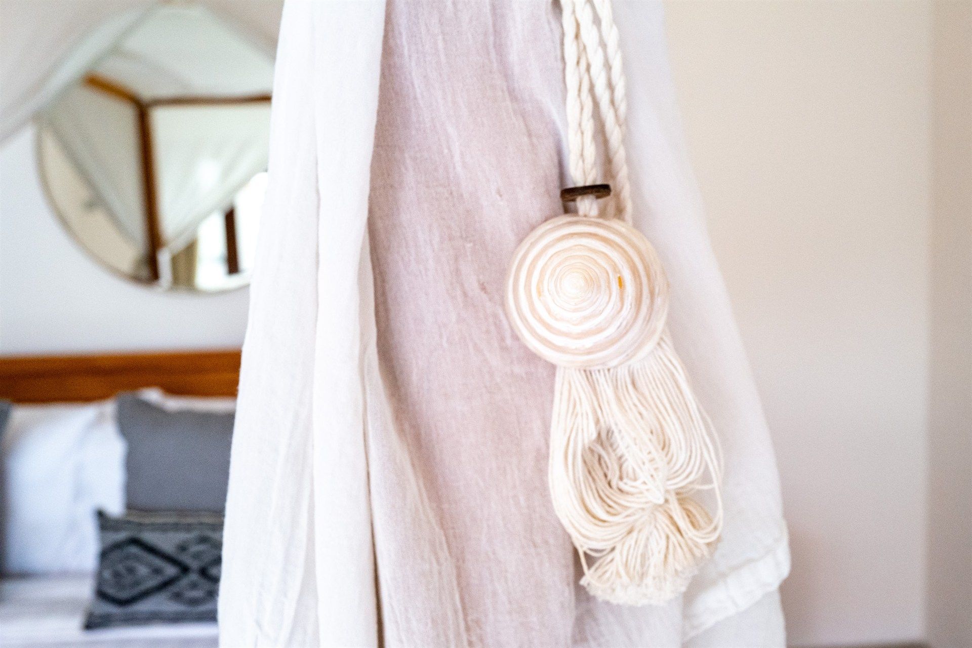White curtain tied back with a woven rope and shell tassel, bedroom setting.