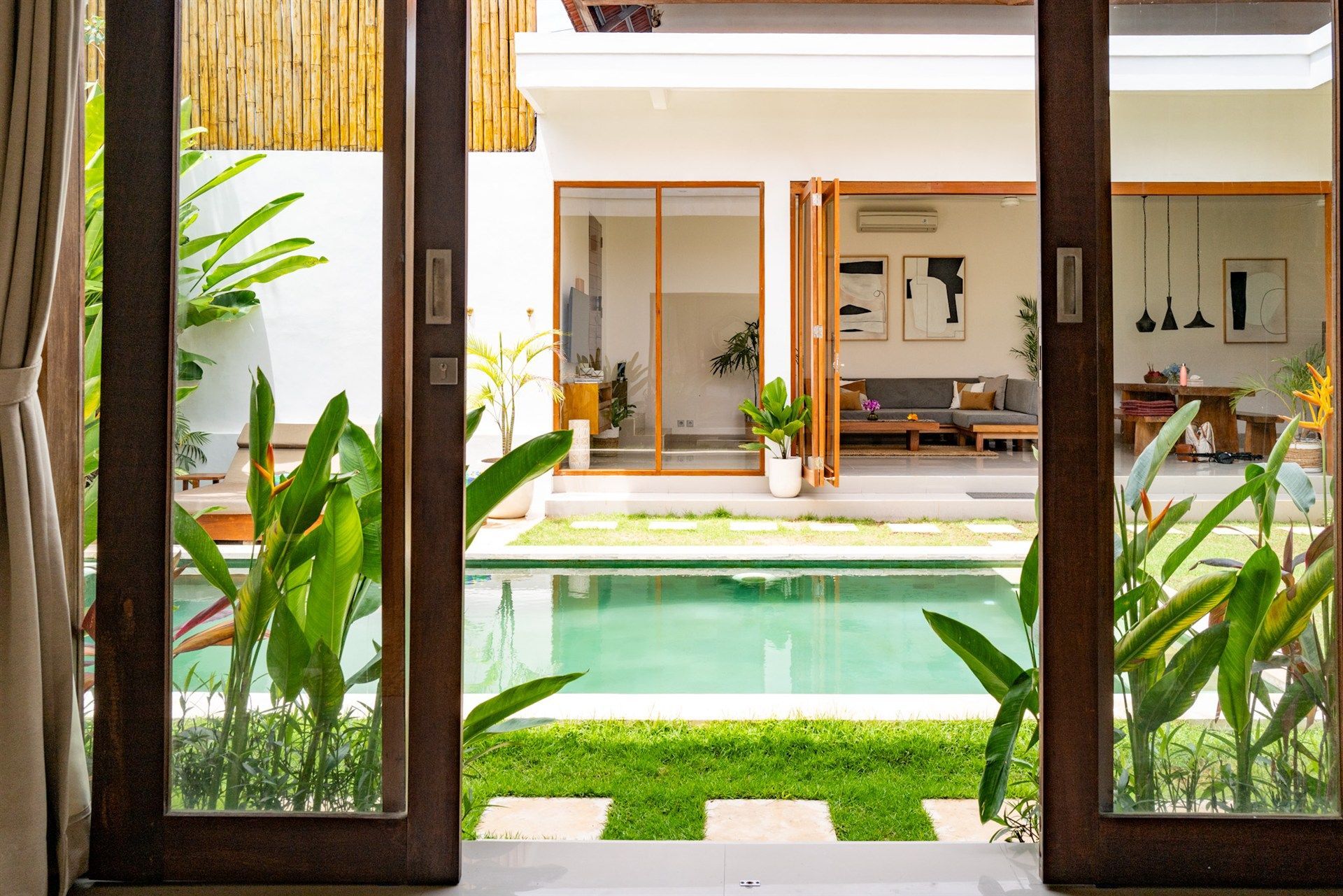 View through open doors to pool, tropical plants, and house with open doors and minimal decor.