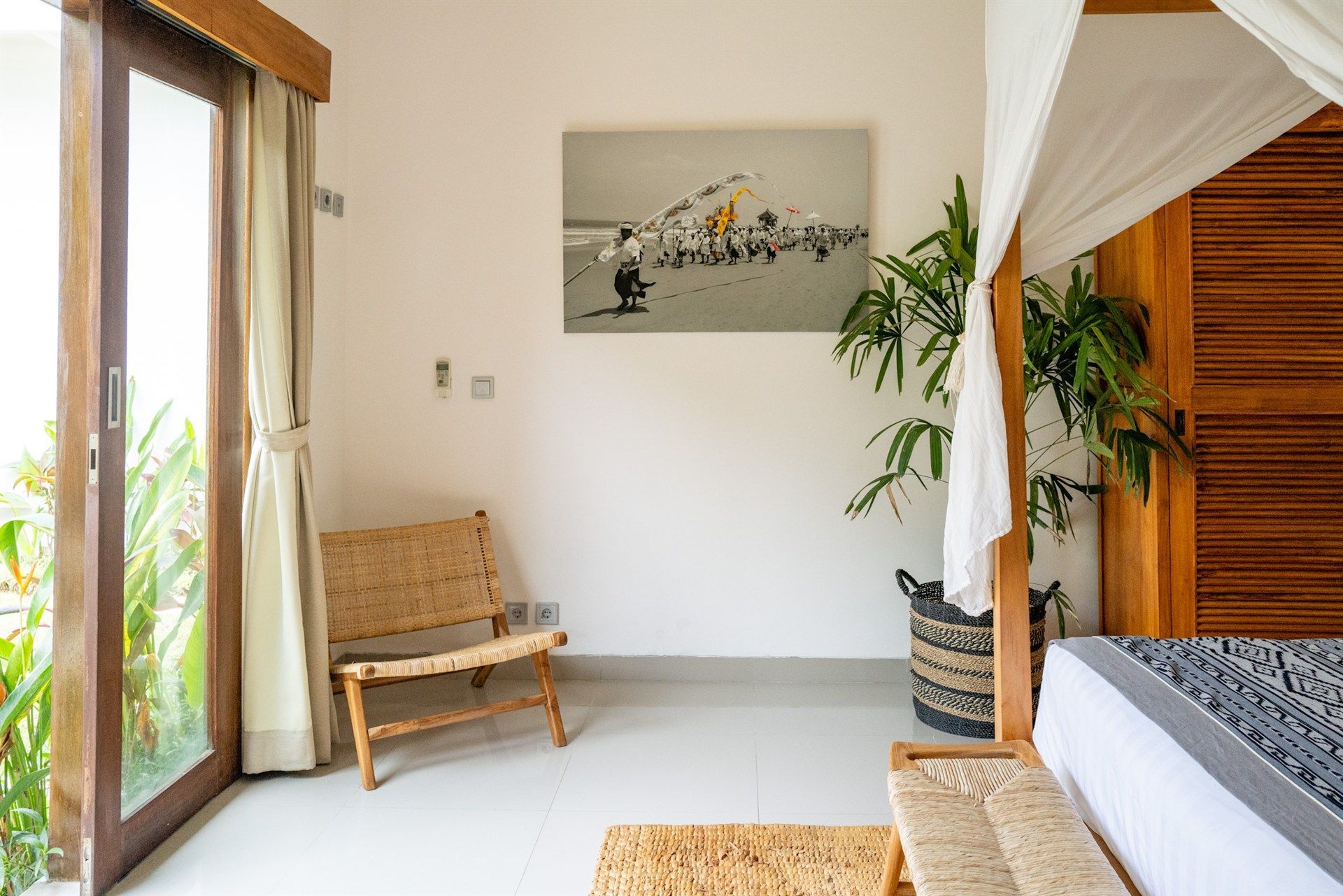 Bedroom interior with a woven chair, sliding glass door, and a bed with canopy.