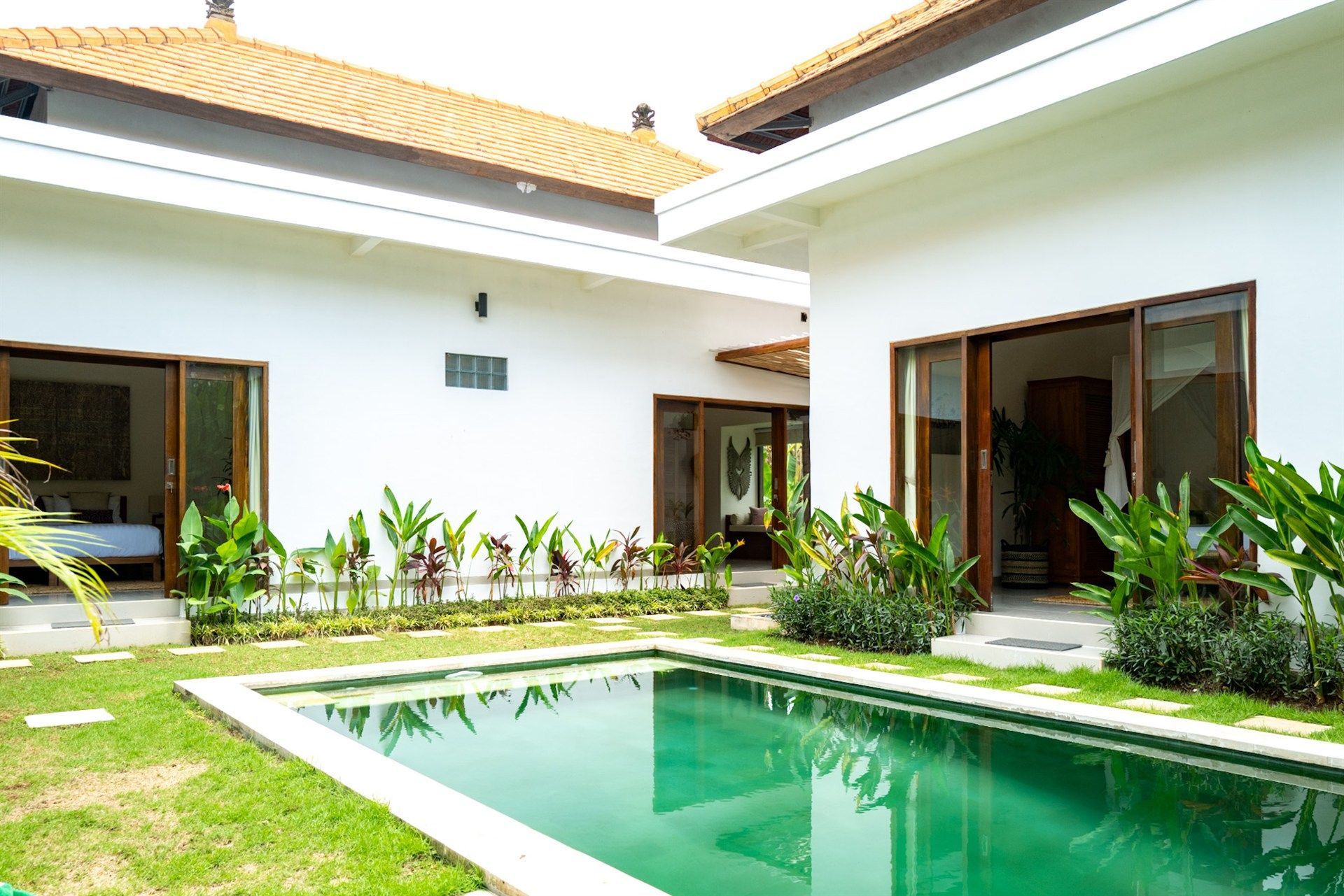 Exterior of a white villa with a rectangular swimming pool, surrounded by greenery and a lawn.