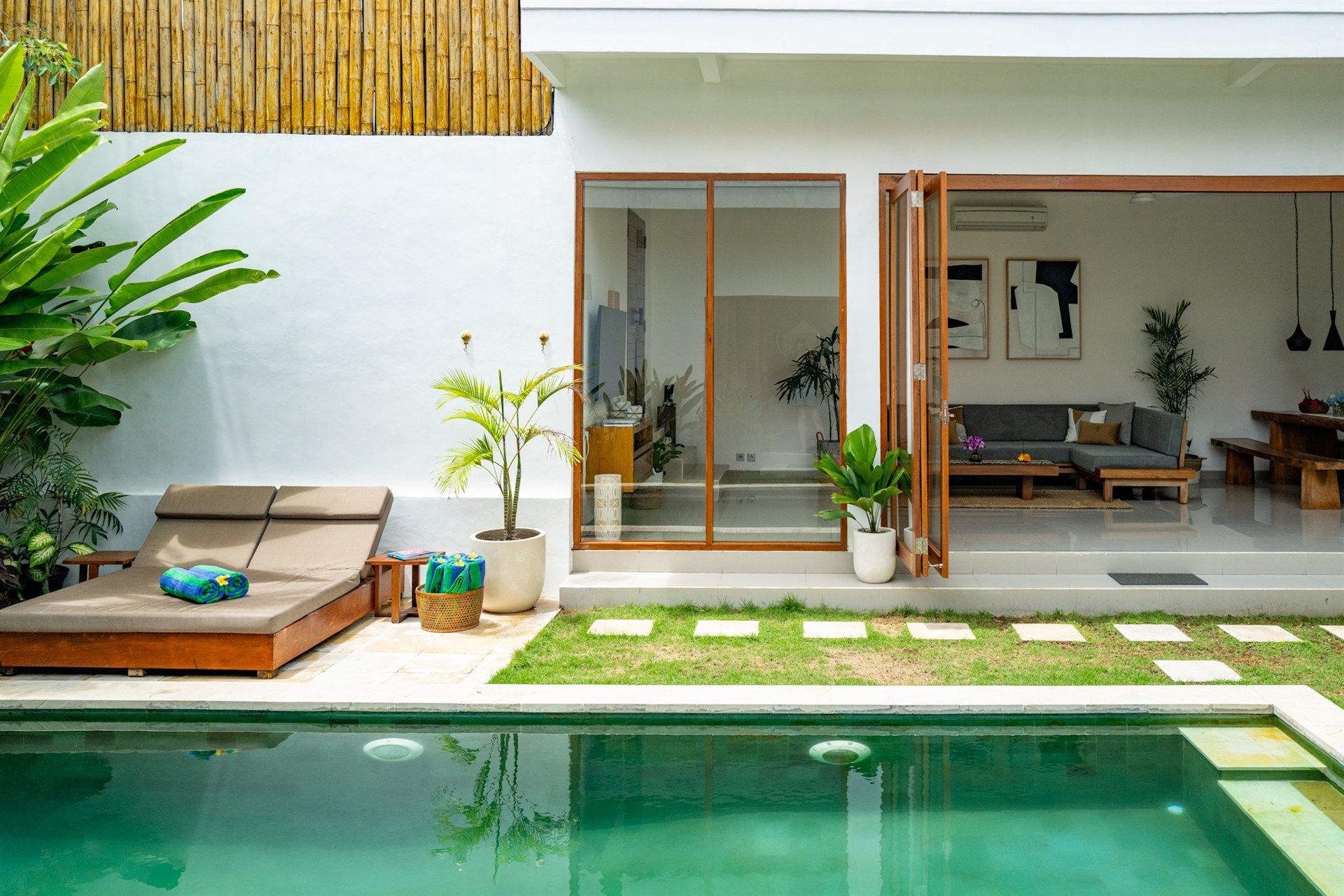 Poolside villa with pool, lounge chairs, and open doors to a living area.
