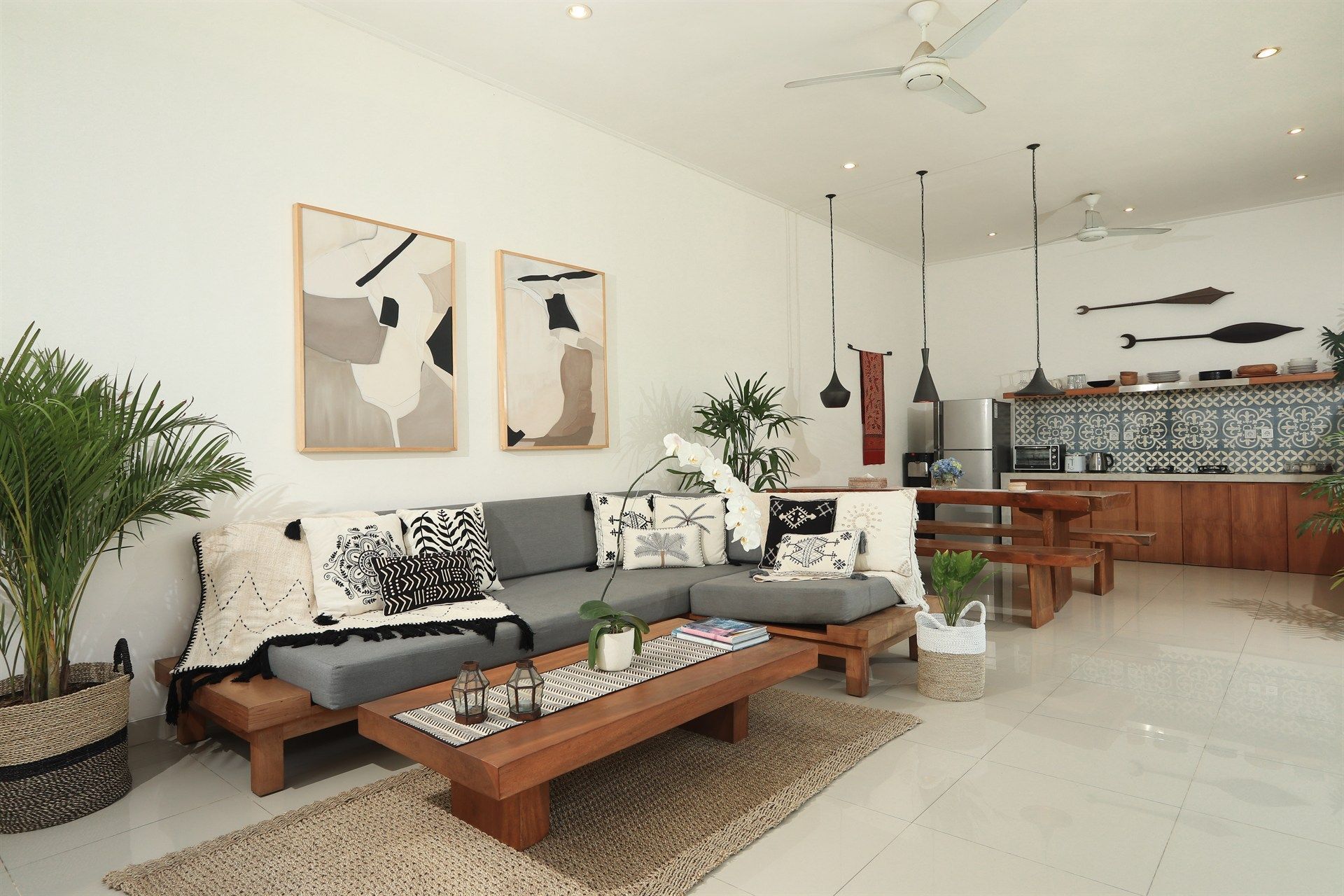 Living room with gray sectional, wooden table, artwork, and open kitchen.
