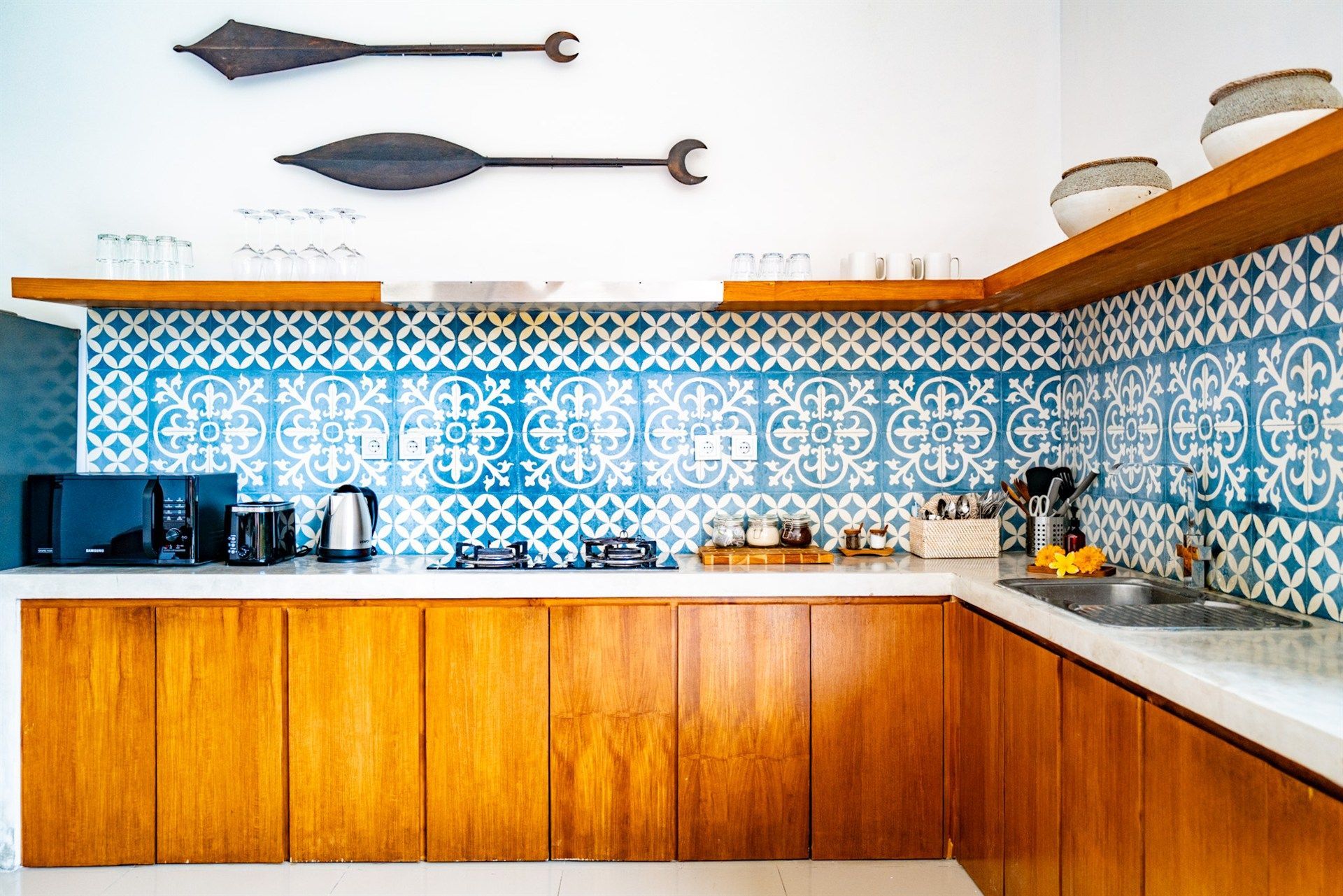 Kitchen with blue patterned tile backsplash, wood cabinets, and white countertops.