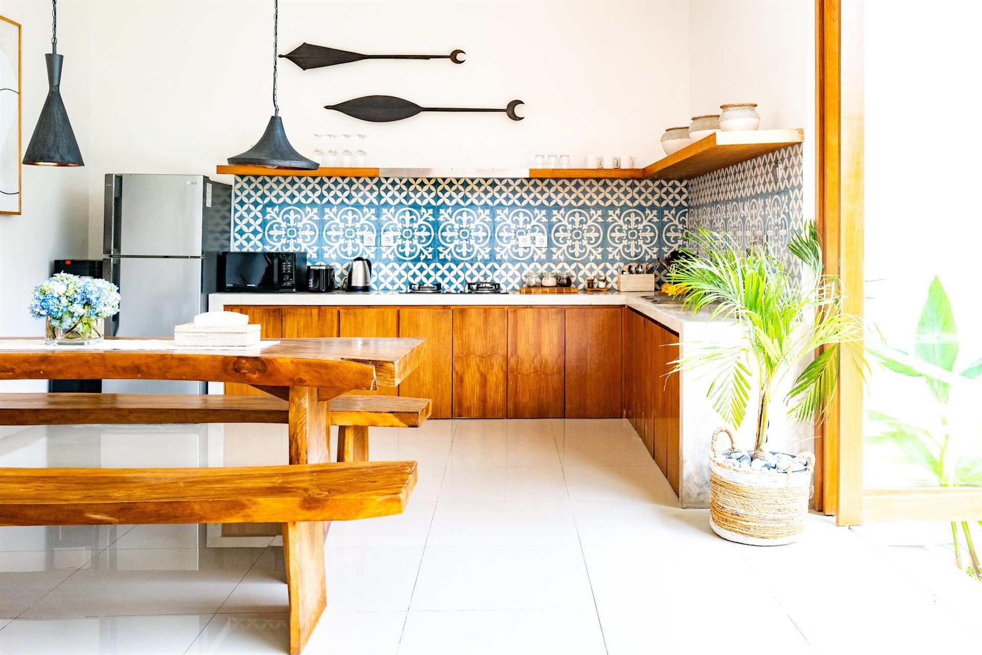 Wooden kitchen with bench seating, blue tile backsplash, wooden cabinets, and a potted plant.