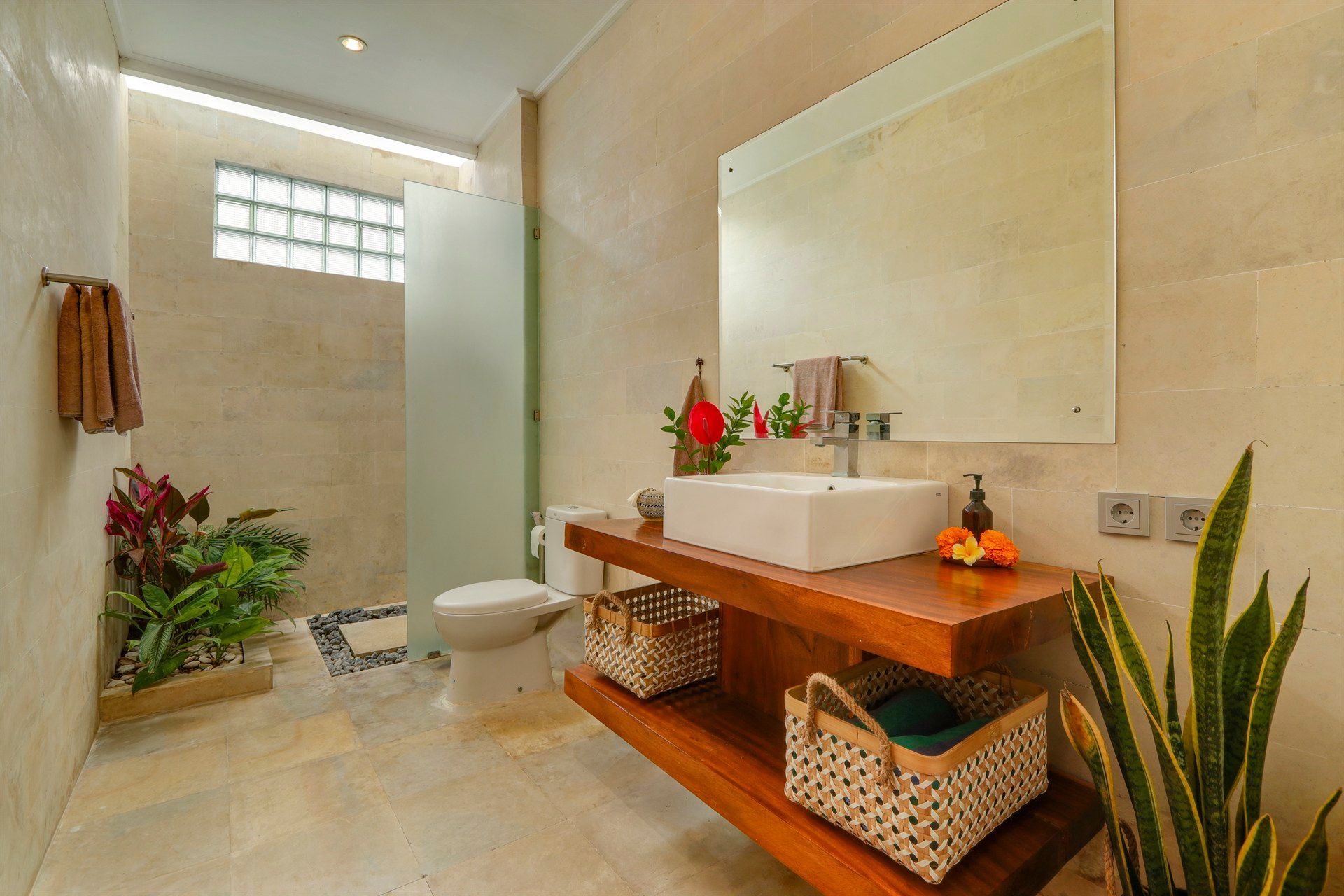 Bathroom with wooden vanity, white sink, beige walls, and plants.