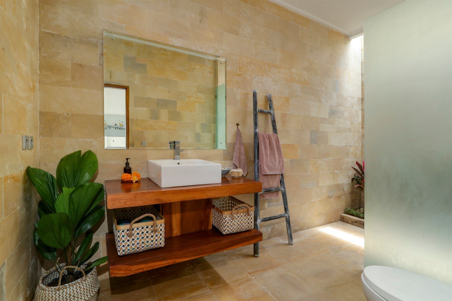 Bathroom with stone walls, wooden vanity, rectangular mirror, and a potted plant.