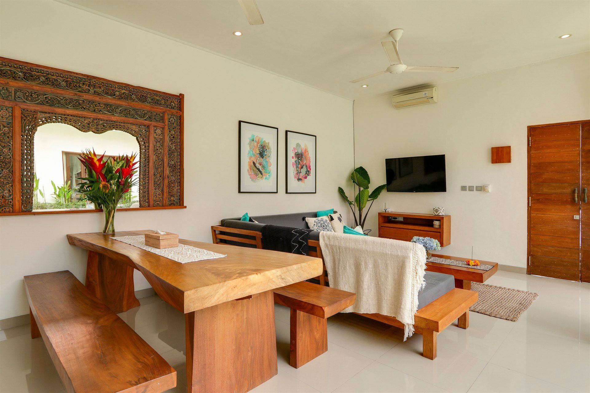 Living room with wooden furniture, dining table with benches, sofa, and TV against white walls.