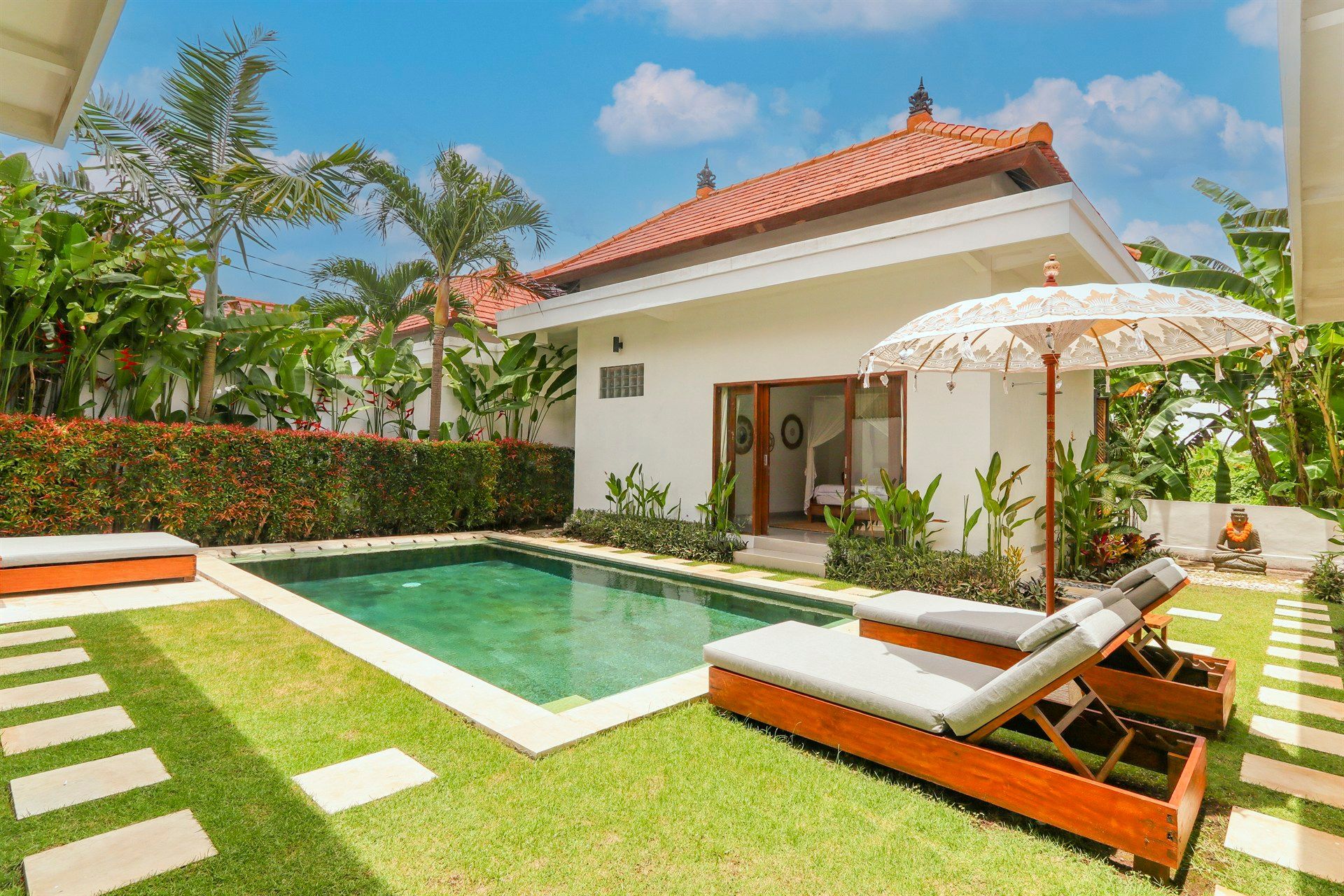 Villa exterior with pool, lounge chairs, and traditional Balinese roof in a tropical setting.