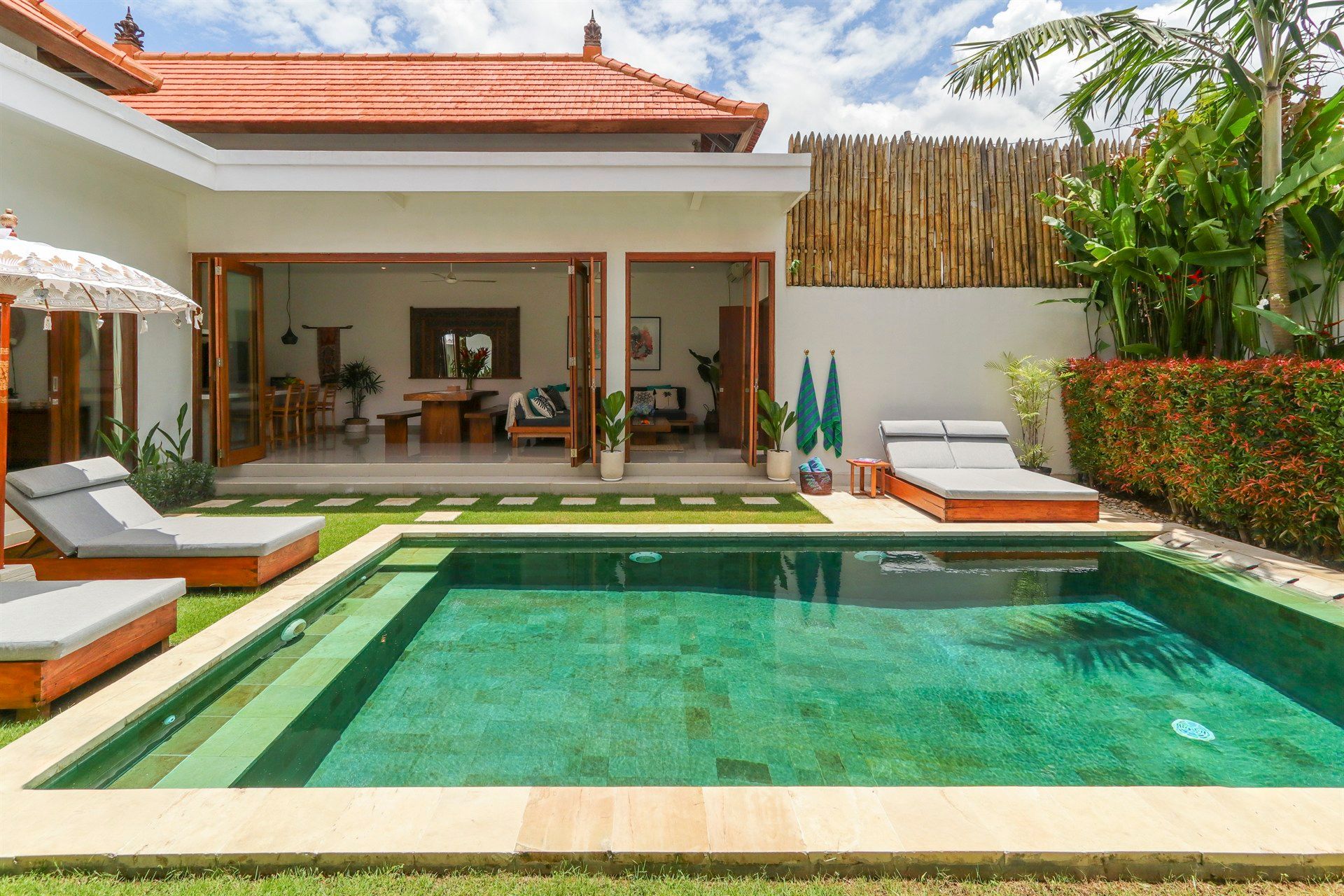 Villa with a teal pool, lounge chairs, and open doors to the interior.