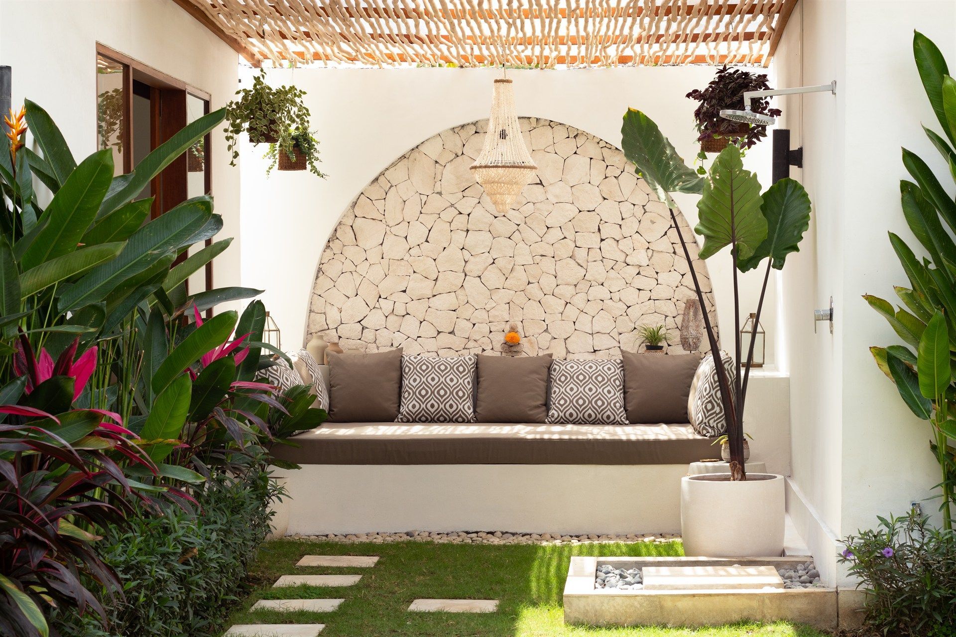 Outdoor seating nook with stone wall, cushions, and plants.
