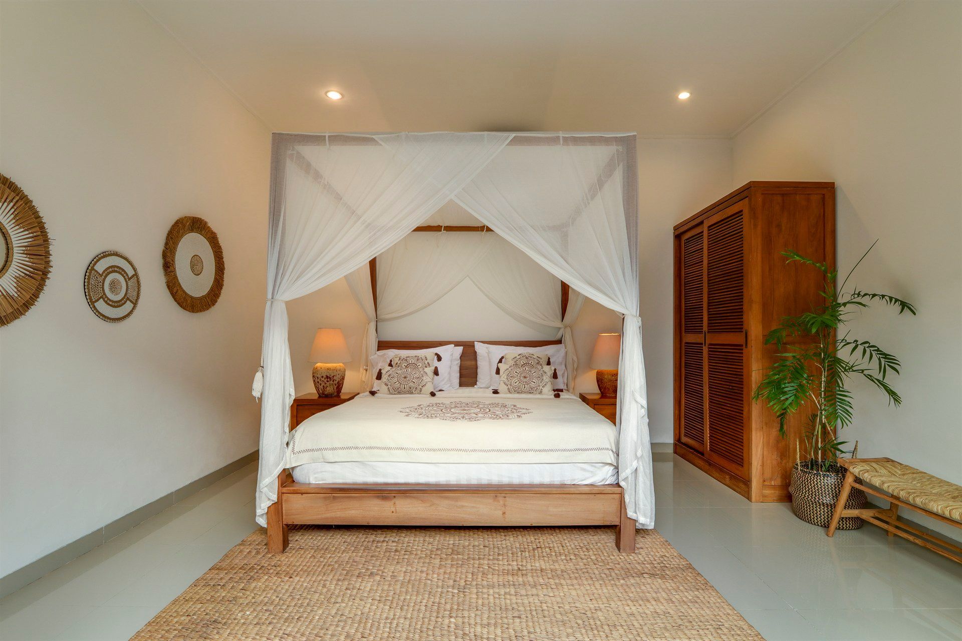 Bedroom with canopy bed, wooden furniture, woven rug, and wall art.