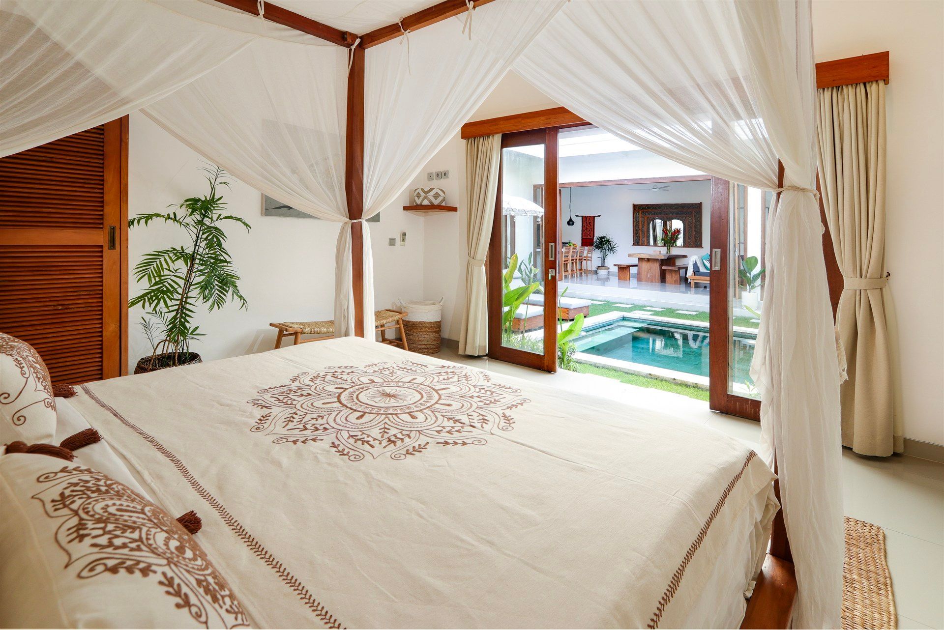 Bedroom with canopy bed, open doors to pool area. Light and airy interior with white linens and wood accents.